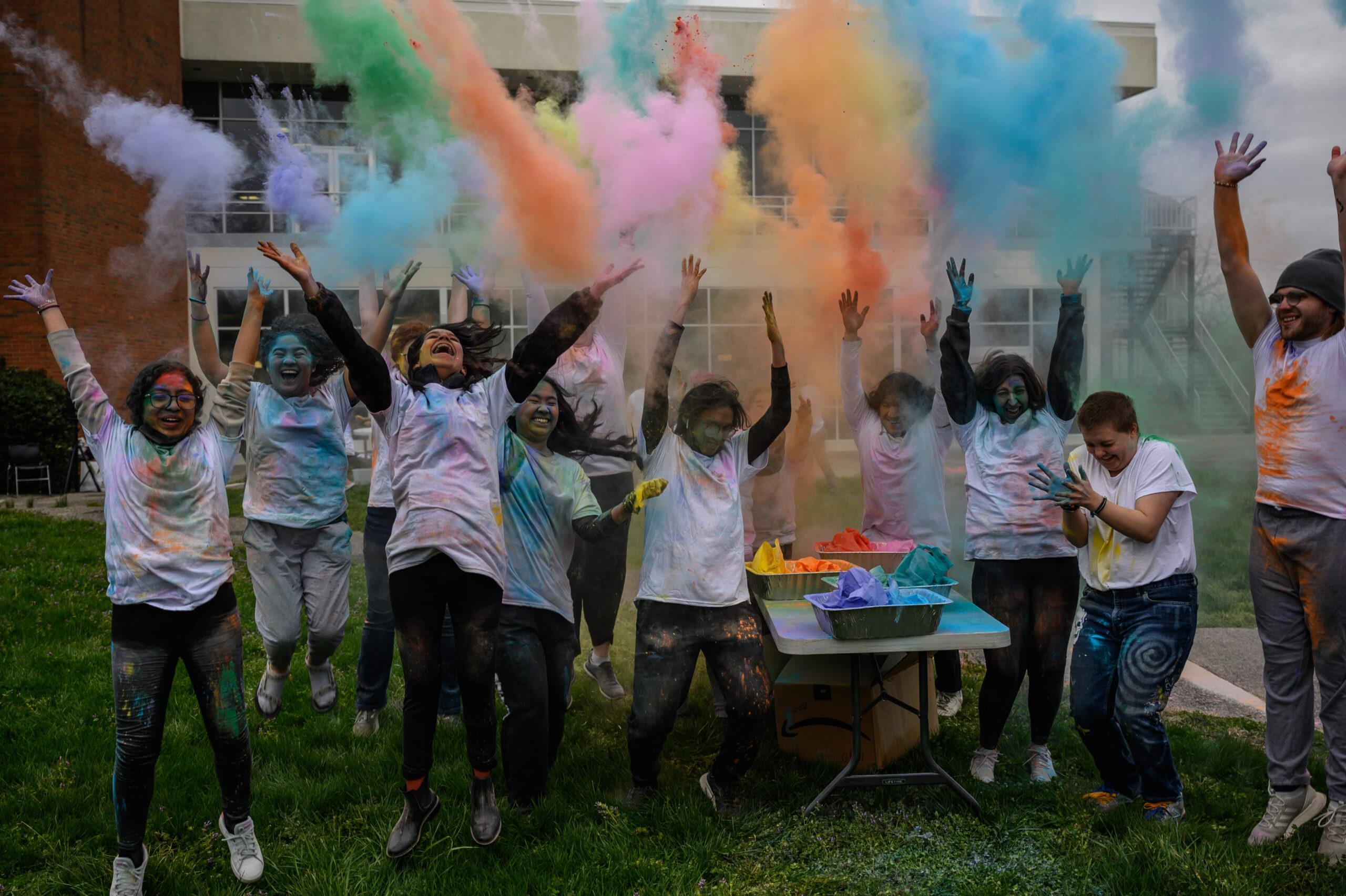 A group of students throwing colored powder into the air in celebration of Holi.