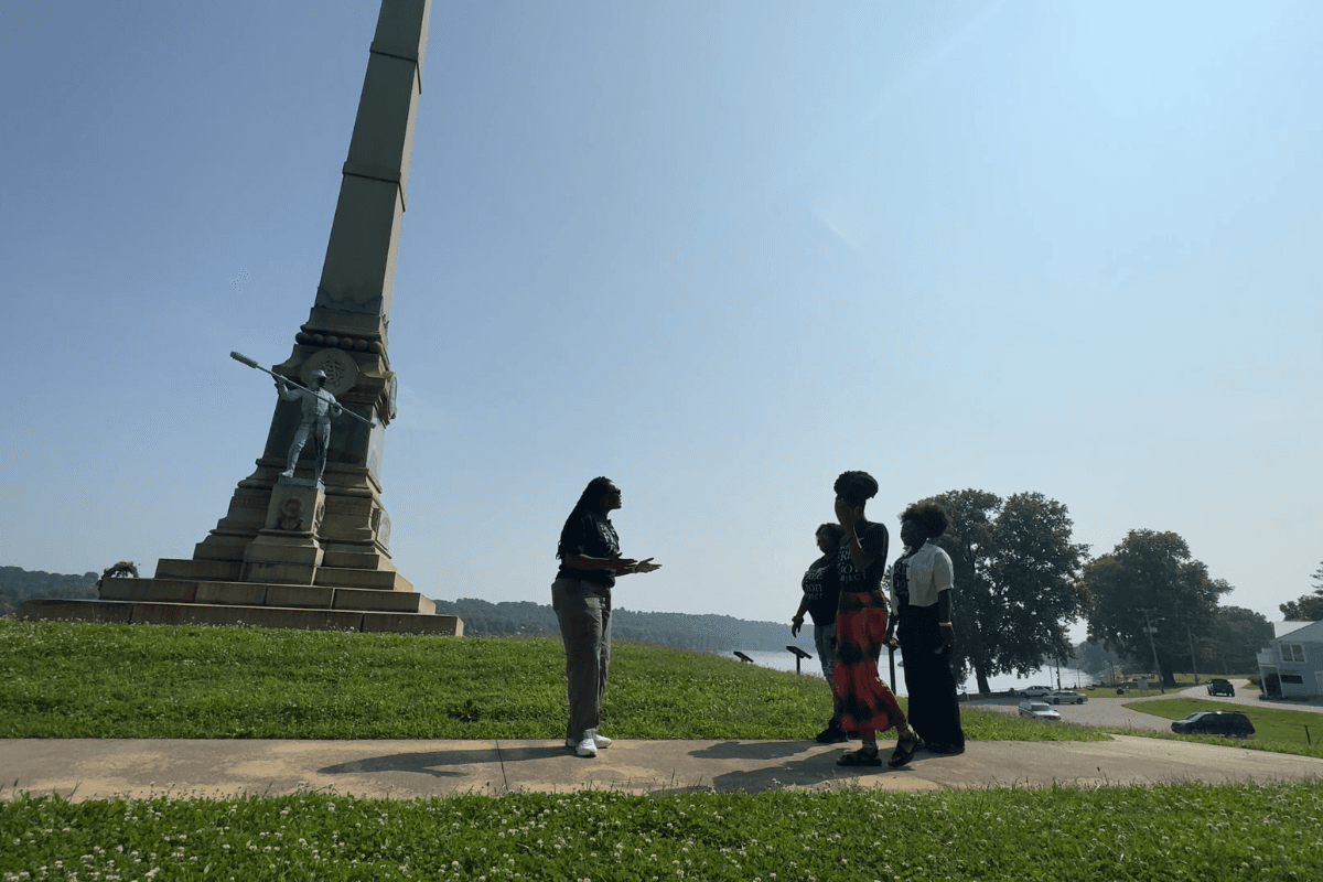 A group of four women stand outside on a sunny day in front of a historic monument.