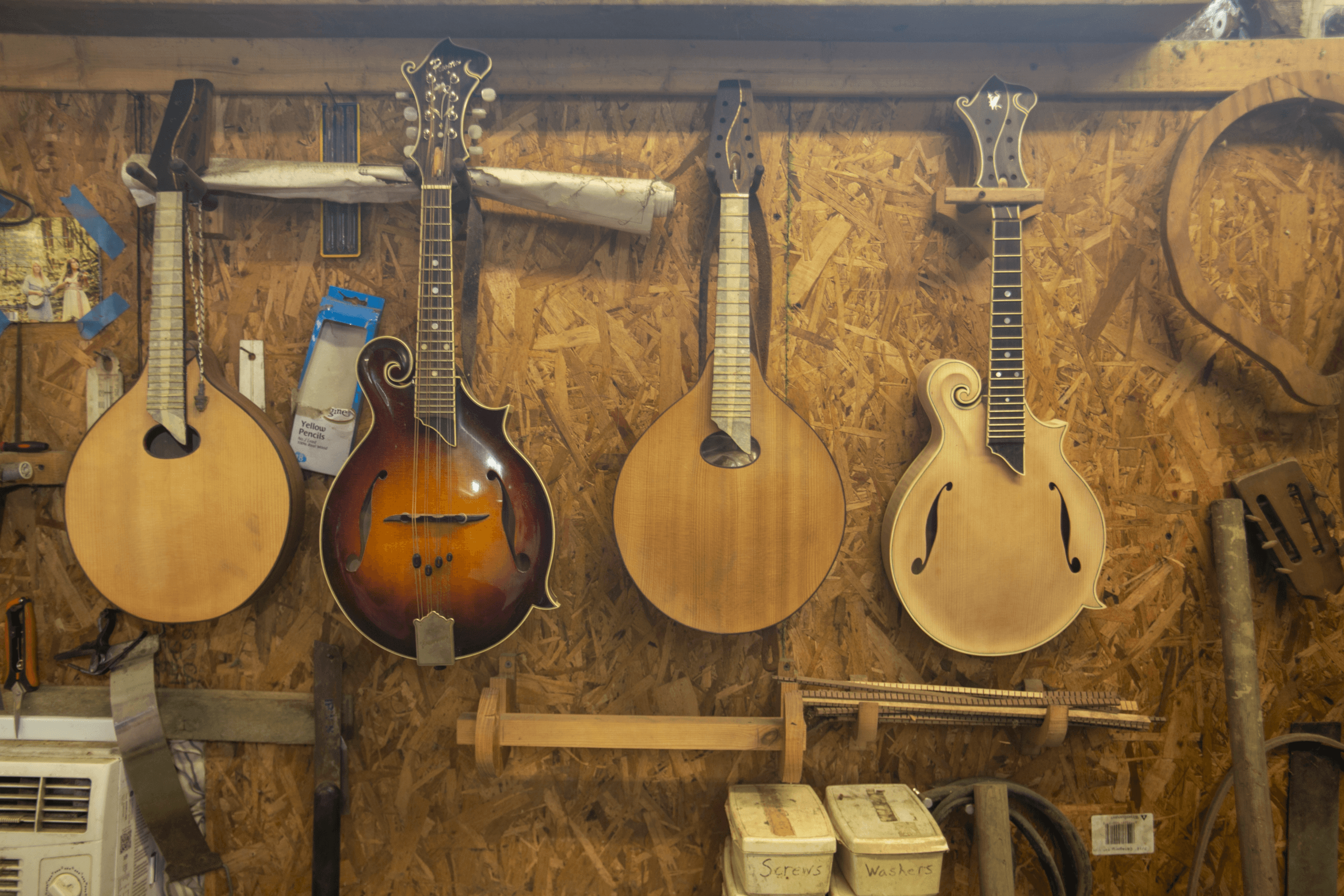 Four wooden mandolins hanging against a wall inside a woodworking studio.